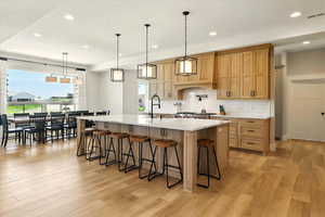 Kitchen with recessed lighting, a large island with sink, a breakfast bar area, light wood-style floors, and decorative backsplash