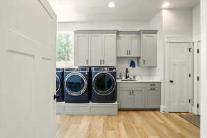 Laundry area featuring light wood-type flooring, separate washer and dryer, cabinet space, and recessed lighting
