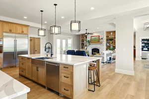 Kitchen featuring appliances with stainless steel finishes, a fireplace, pendant lighting, a large island with sink, and recessed lighting