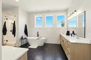 Full bath featuring tile walls, vanity, dark tile patterned floors, wainscoting, and a soaking tub