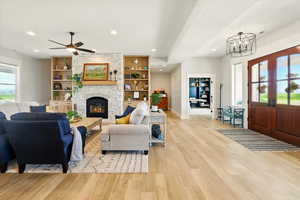Living room featuring light wood finished floors, a stone fireplace, recessed lighting, a ceiling fan, and french doors