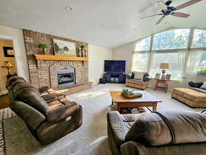 Carpeted living room with lofted ceiling, a brick fireplace, and ceiling fan