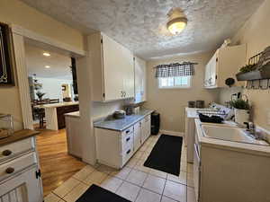 Kitchen featuring a textured ceiling, light tile patterned floors, white cabinetry, washing machine and dryer, and light countertops
