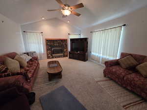 Carpeted living room with a stone fireplace, vaulted ceiling, and ceiling fan
