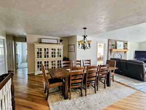 Dining area with a fireplace, healthy amount of natural light, dark wood finished floors, a textured ceiling, and a chandelier