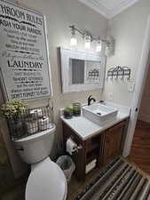 Half bath featuring vanity, crown molding, and wood finished floors