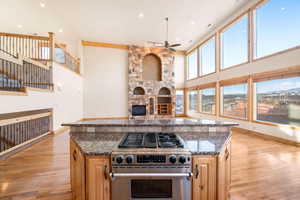 Kitchen featuring dark stone counters, stainless steel range, a fireplace, a towering ceiling, and light wood-type flooring