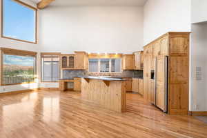 Kitchen with a breakfast bar area, a high ceiling, paneled fridge, light wood-type flooring, and beamed ceiling