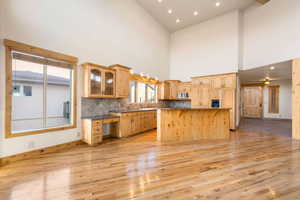 Kitchen with a breakfast bar area, a center island, glass insert cabinets, light wood-style flooring, and a high ceiling