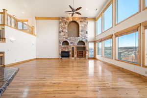 Unfurnished living room with light wood-type flooring, a fireplace, a towering ceiling, and a ceiling fan