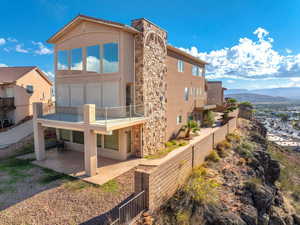 Rear view of house with stone siding, a patio, stucco siding, a mountain view, and a balcony