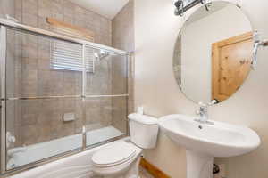 Full bath featuring toilet and bath / shower combo with glass door