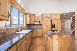 Kitchen with light brown cabinetry, light wood finished floors, backsplash, and dark stone counters