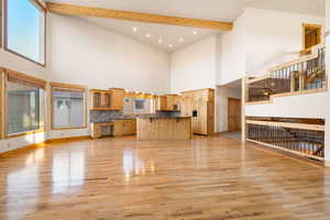 Unfurnished living room featuring light wood-style flooring, beam ceiling, a high ceiling, and recessed lighting