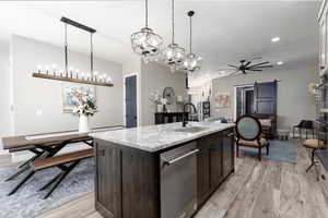 Kitchen with a barn door, light stone countertops, light wood-type flooring, a center island with sink, and recessed lighting