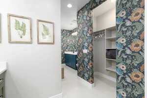 Full bathroom with vanity, light tile patterned floors, wallpapered walls, and a walk in closet