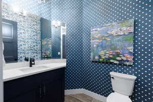 Half bathroom featuring wallpapered walls and vanity