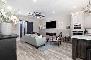 Living area with a barn door, light wood finished floors, recessed lighting, and a glass covered fireplace