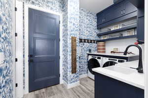 Kitchen with blue cabinetry, light wood-style flooring, wallpapered walls, open shelves, and washer and dryer