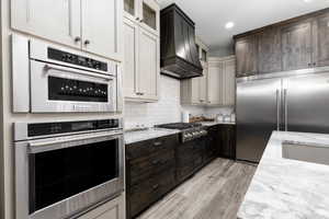 Kitchen with light stone counters, glass insert cabinets, stainless steel appliances, tasteful backsplash, and recessed lighting