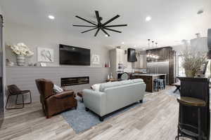 Living room with light wood-style flooring, recessed lighting, ceiling fan, a glass covered fireplace, and a barn door