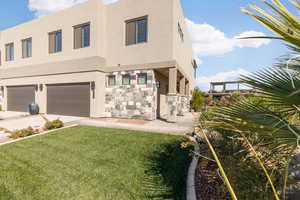 Rear view of house featuring stucco siding, a yard, and stone siding
