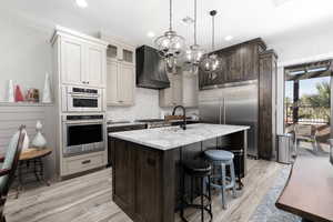 Kitchen with a kitchen bar, dark brown cabinetry, light wood finished floors, glass insert cabinets, and a kitchen island with sink