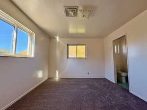 Unfurnished bedroom featuring dark colored carpet and ensuite bath