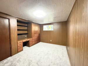 Unfurnished bedroom featuring wooden walls, light carpet, a closet, a textured ceiling, and built in desk