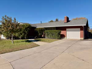 Single story home featuring a front yard, brick siding, a chimney, an attached garage, and driveway