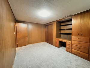 Unfurnished bedroom with a textured ceiling, a closet, built in desk, light carpet, and wooden walls