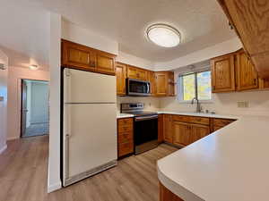 Kitchen with brown cabinets, appliances with stainless steel finishes, light countertops, a textured ceiling, and light wood-style floors