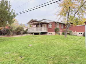 Back of house featuring a yard, a wooden deck, and brick siding