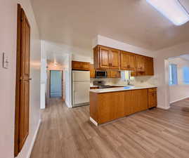 Kitchen with brown cabinetry, stainless steel appliances, light countertops, a peninsula, and light wood-style flooring