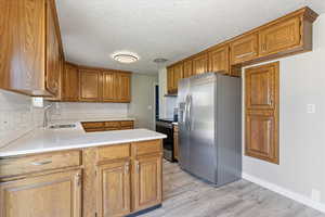 Kitchen with a peninsula, brown cabinetry, stainless steel appliances, tasteful backsplash, and light countertops