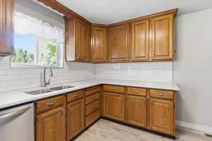 Kitchen featuring decorative backsplash, brown cabinets, stainless steel dishwasher, light stone counters, and a textured ceiling