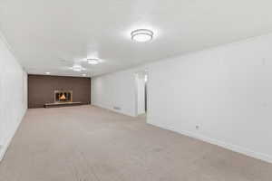 Below grade area featuring light carpet, a brick fireplace, a textured ceiling, ornamental molding, and wooden walls