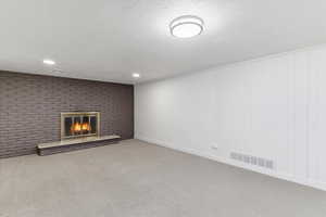 Unfurnished living room featuring carpet flooring, a textured ceiling, a brick fireplace, brick wall, and recessed lighting