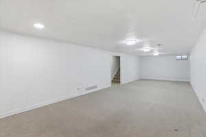 Finished below grade area with a textured ceiling, light colored carpet, and stairway