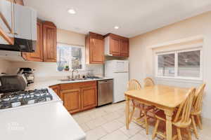 Kitchen with brown cabinets, light countertops, stainless steel dishwasher, light tile patterned floors, and recessed lighting