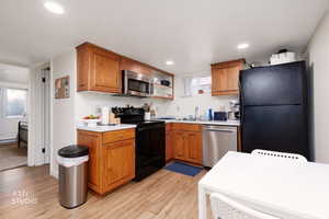 Kitchen with brown cabinetry, light countertops, black appliances, recessed lighting, and a textured ceiling