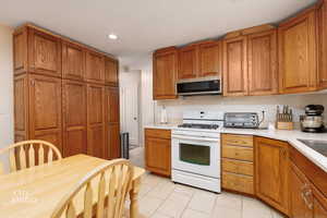 Kitchen featuring brown cabinets, white range with gas stovetop, light countertops, and recessed lighting
