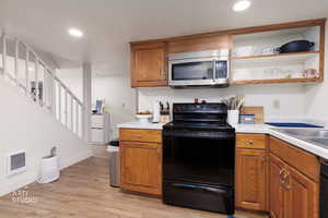 Kitchen featuring black electric range oven, stainless steel microwave, open shelves, light countertops, and brown cabinetry