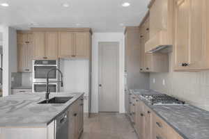 Kitchen with tasteful backsplash, dark stone countertops, appliances with stainless steel finishes, a kitchen island with sink, and recessed lighting