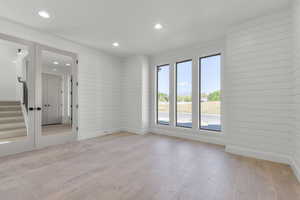 Spare room featuring light wood-style flooring, stairs, recessed lighting, and wood walls