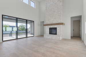 Unfurnished living room featuring a towering ceiling, light wood-type flooring, and a stone fireplace