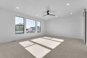Empty room with a barn door, recessed lighting, light colored carpet, and a ceiling fan