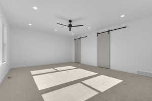 Unfurnished bedroom with a barn door, light carpet, recessed lighting, and ceiling fan