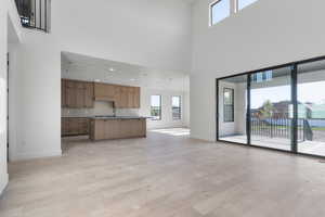Unfurnished living room featuring plenty of natural light, a towering ceiling, and light wood finished floors