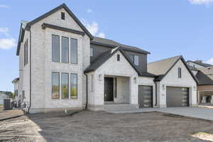 View of front of property with driveway, a shingled roof, stone siding, brick siding, and a garage